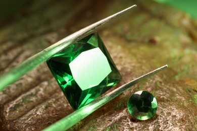 Photo of Tweezers with beautiful green gemstones on stone, closeup