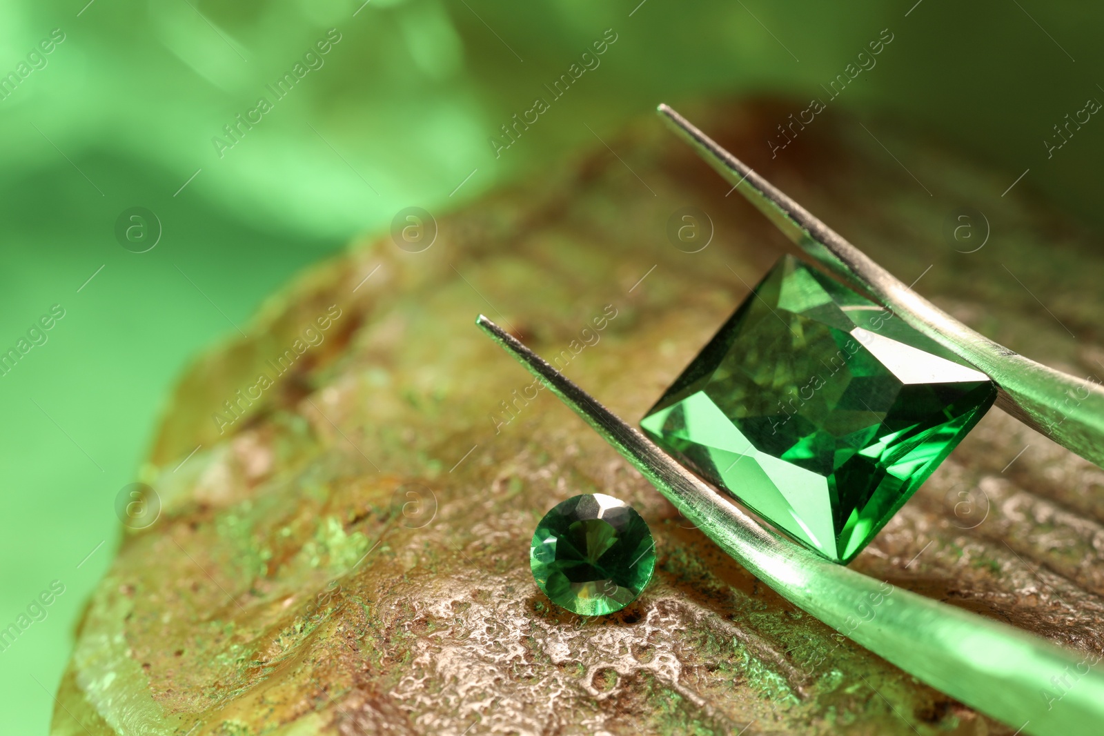 Photo of Tweezers with beautiful green gemstones on stone, closeup. Space for text