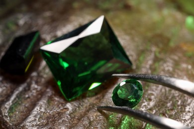 Photo of Tweezers with beautiful green gemstones on stone, closeup