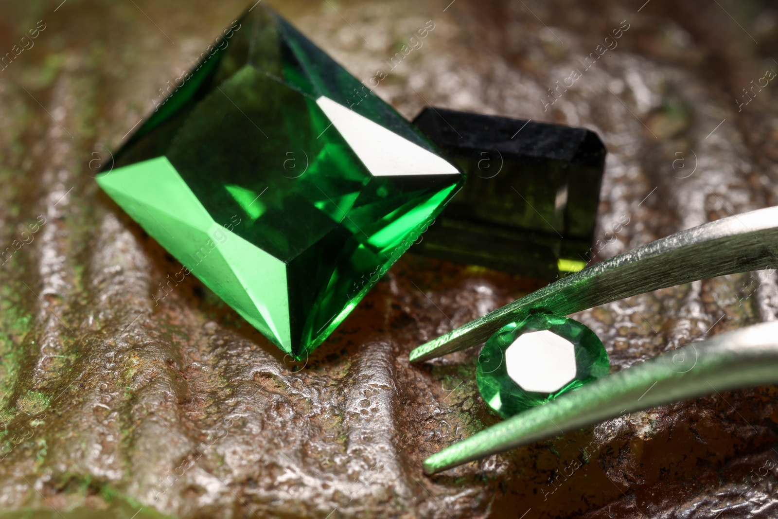 Photo of Tweezers with beautiful green gemstones on stone, closeup