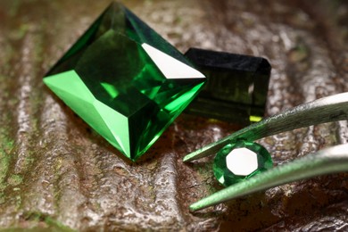 Photo of Tweezers with beautiful green gemstones on stone, closeup