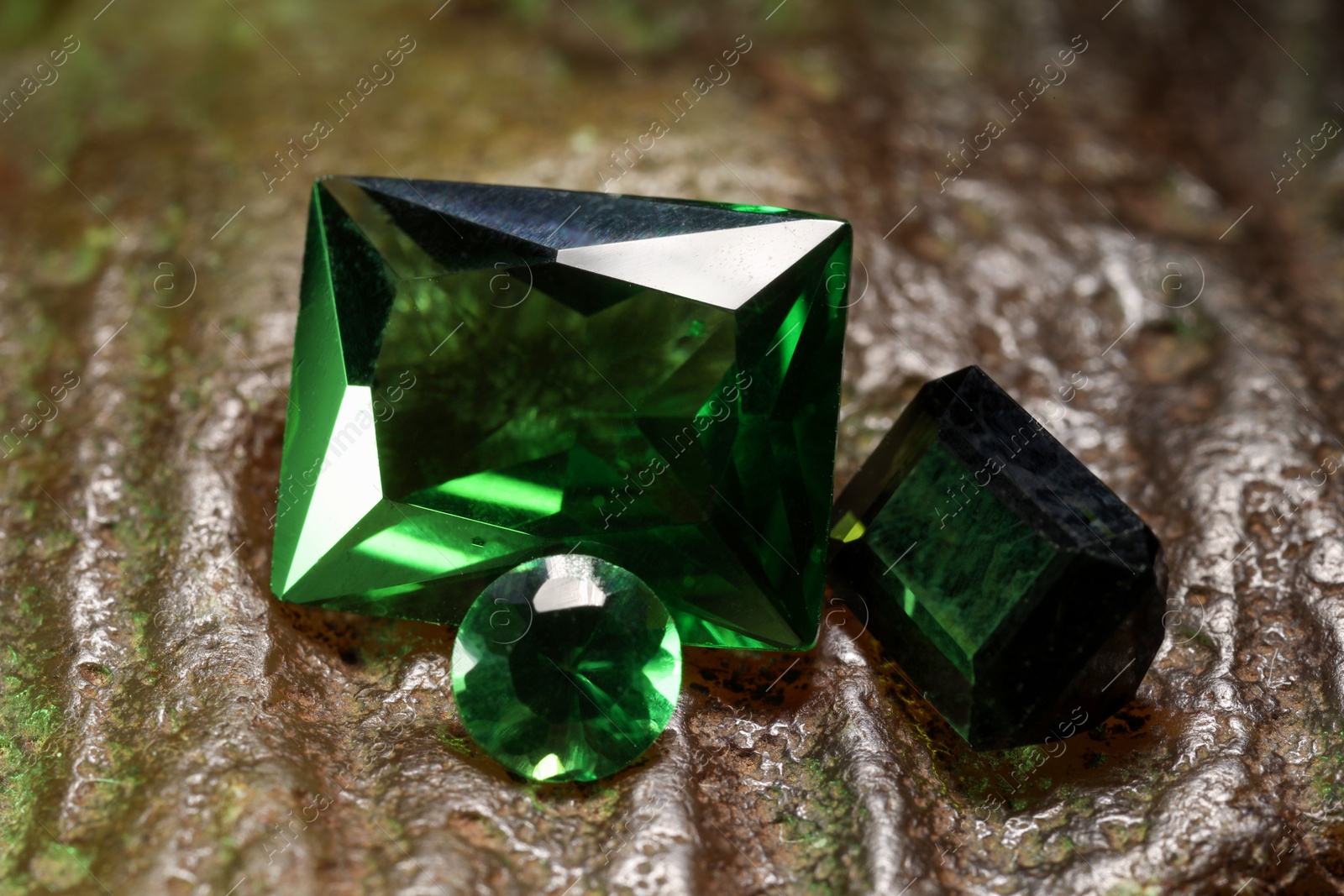 Photo of Beautiful shiny green gemstones on stone, closeup