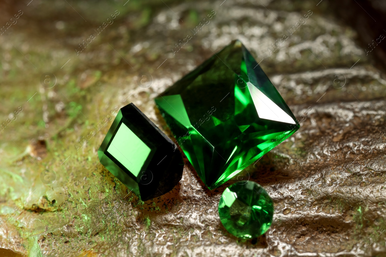 Photo of Beautiful shiny green gemstones on stone, closeup