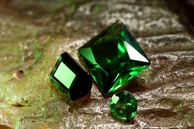 Photo of Beautiful shiny green gemstones on stone, closeup