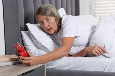 Overslept woman with alarm clock in bed at home