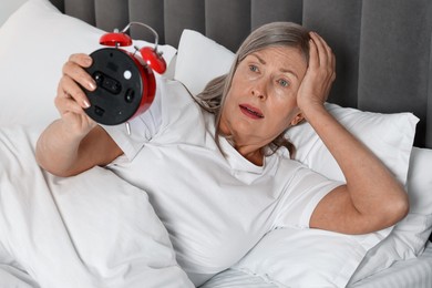 Overslept woman with alarm clock in bed at home