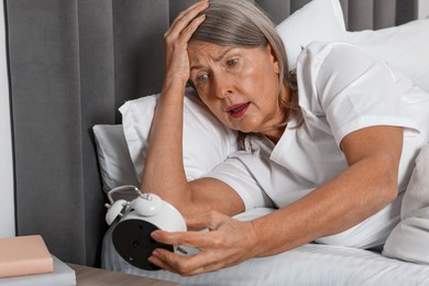 Overslept woman with alarm clock in bed at home