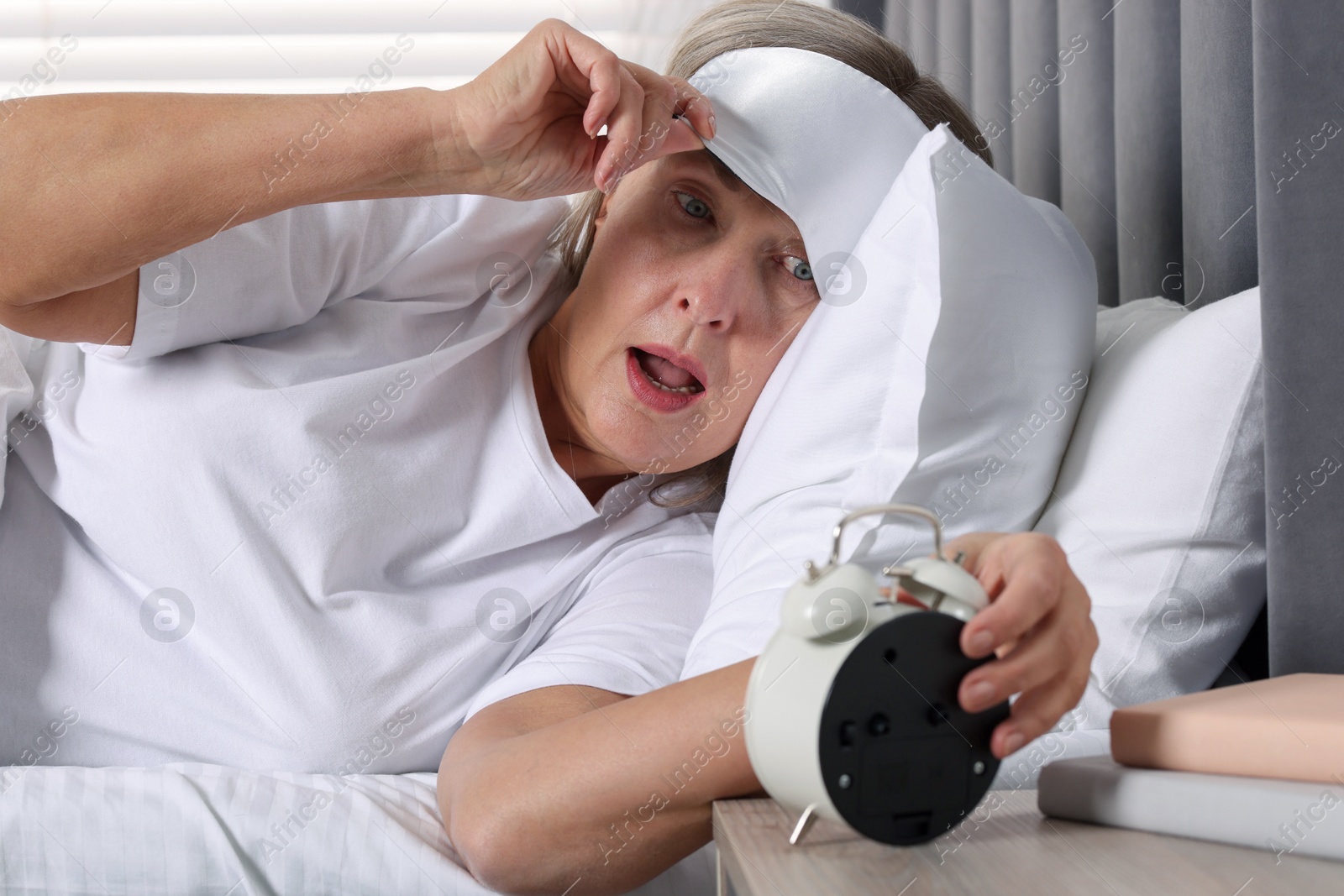 Photo of Overslept woman looking at alarm clock in bed indoors