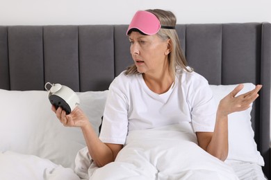 Overslept woman with alarm clock in bed at home