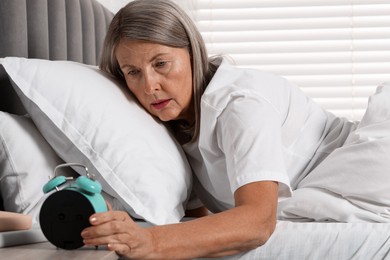 Photo of Overslept woman looking at alarm clock in bed indoors