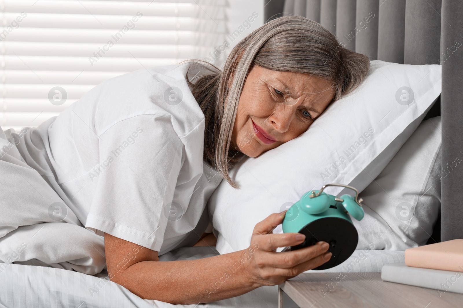 Photo of Overslept woman looking at alarm clock in bed indoors