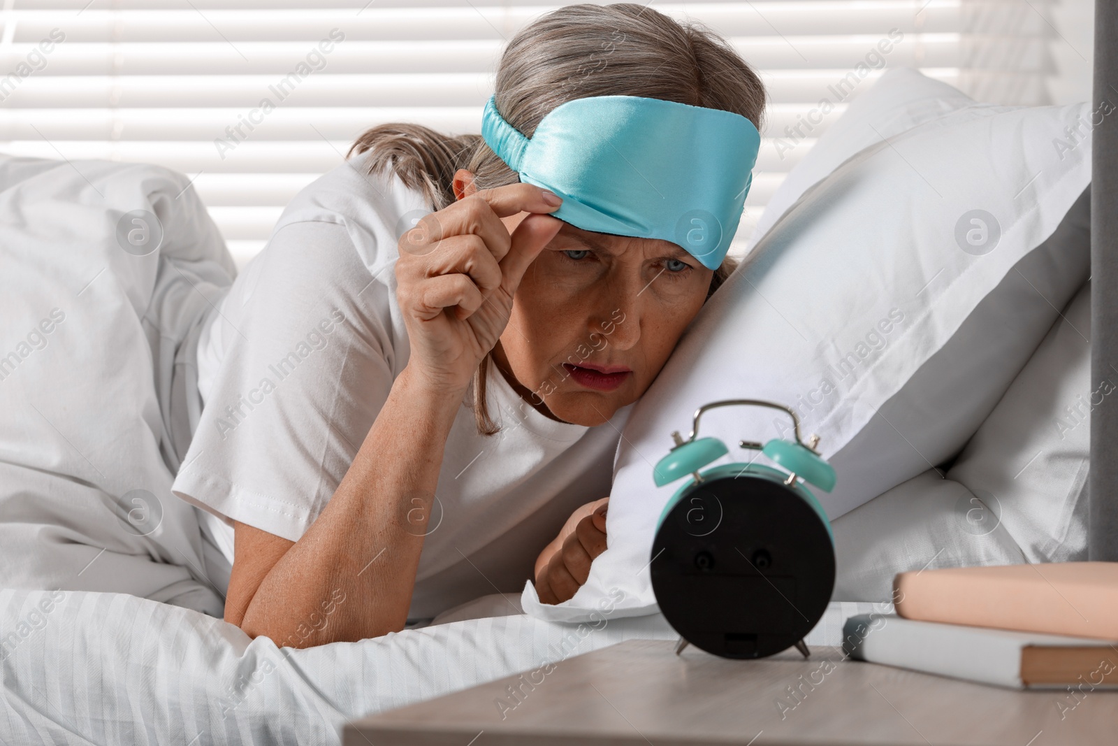 Photo of Overslept woman looking at alarm clock in bed indoors