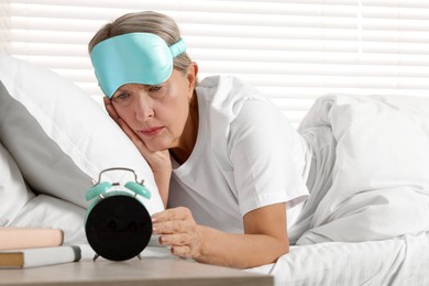 Photo of Overslept woman looking at alarm clock in bed indoors