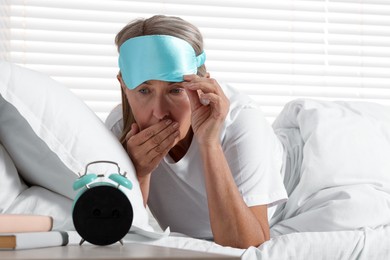 Photo of Overslept woman looking at alarm clock in bed indoors