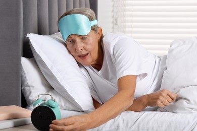 Photo of Overslept woman looking at alarm clock in bed indoors