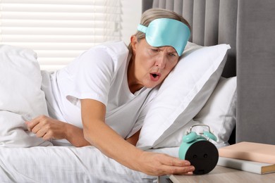 Photo of Overslept woman looking at alarm clock in bed indoors