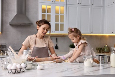 Housewife cooking with her little daughter at marble table in kitchen