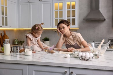 Photo of Tired housewife cooking with her little daughter at marble countertop in kitchen