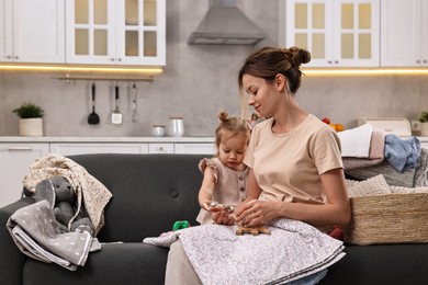 Photo of Housewife with her little daughter among messy laundry on sofa at home