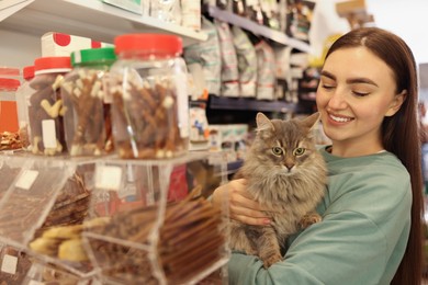 Photo of Woman choosing treats for her cute cat in pet shop