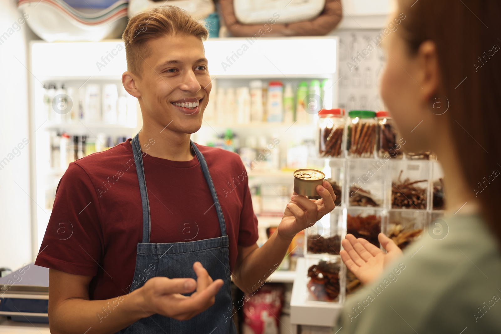 Photo of Pet shop worker helping woman choosing food indoors, selective focus