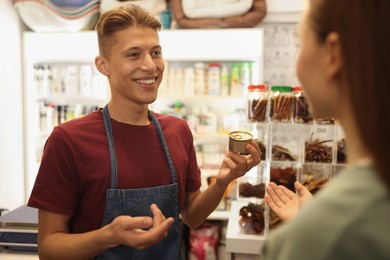 Pet shop worker helping woman choosing food indoors, selective focus