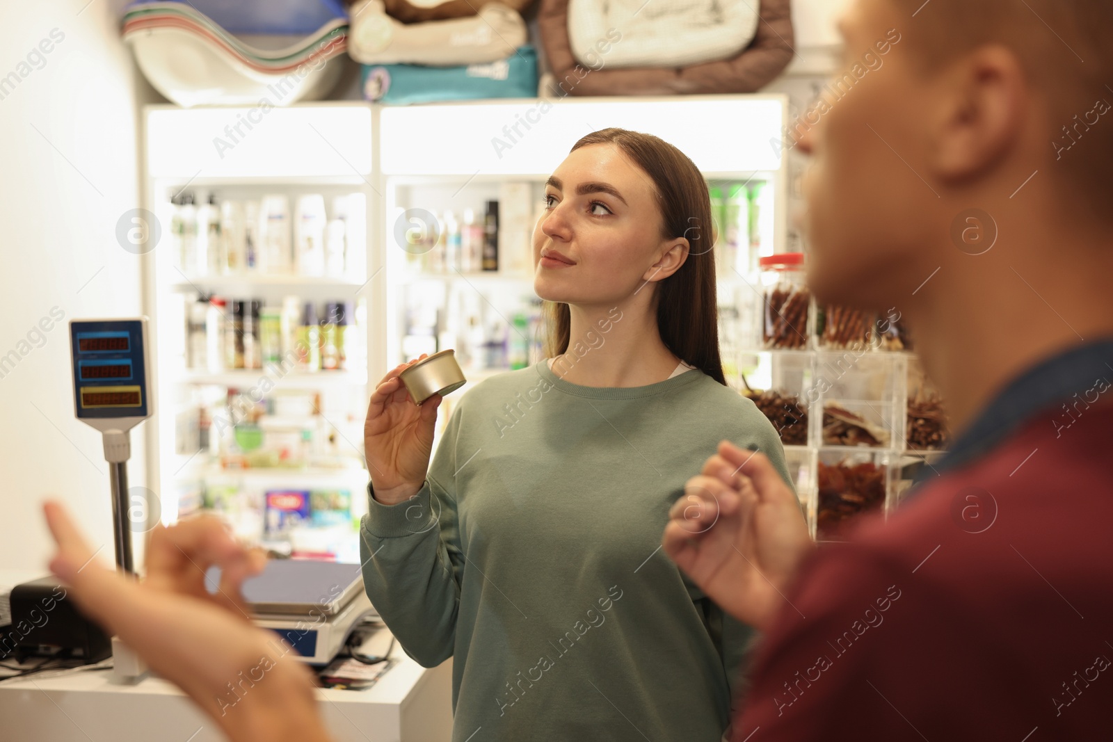 Photo of Pet shop worker helping woman choosing food indoors, selective focus