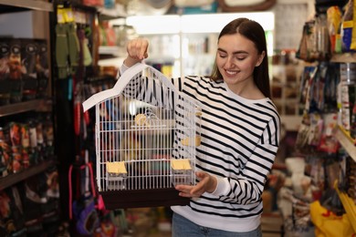 Photo of Smiling woman with bird cage in pet shop