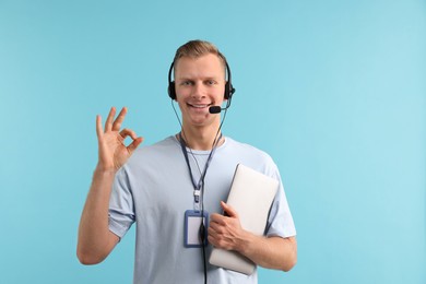 Technical support call center. Smiling operator with laptop showing ok gesture on light blue background