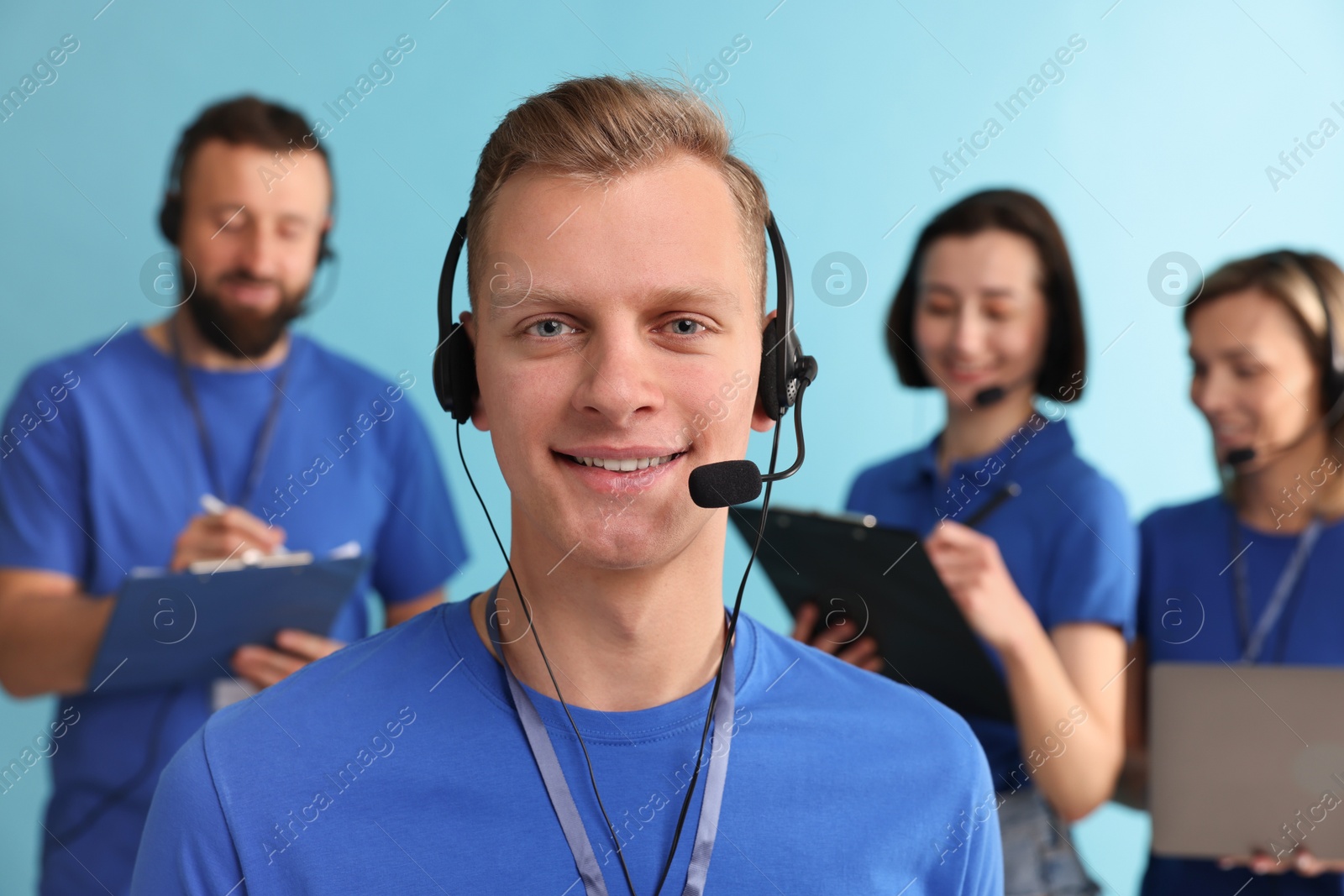 Photo of Technical support call center. Team of friendly operators working on light blue background