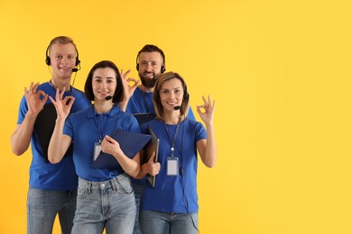 Photo of Technical support call center. Team of friendly operators showing ok gesture on yellow background. Space for text