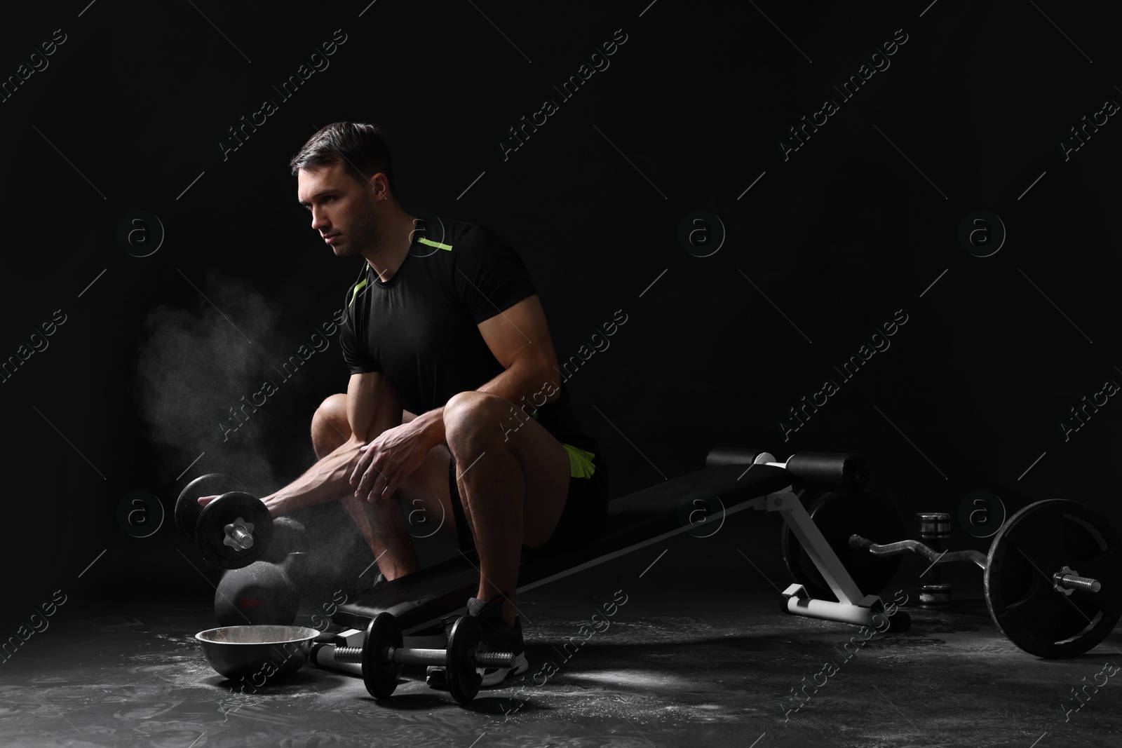 Photo of Man with talcum powder on hands training with barbell against black background