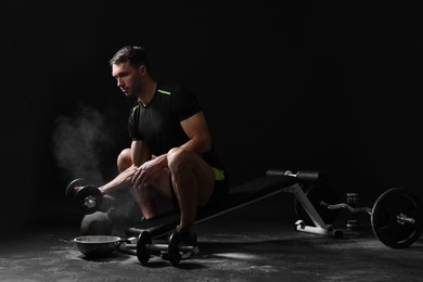 Photo of Man with talcum powder on hands training with barbell against black background