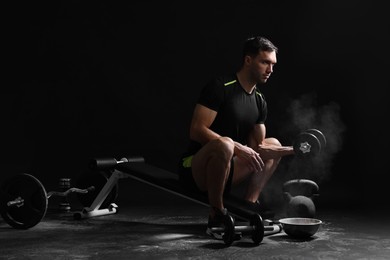 Photo of Man with talcum powder on hands training with barbell against black background