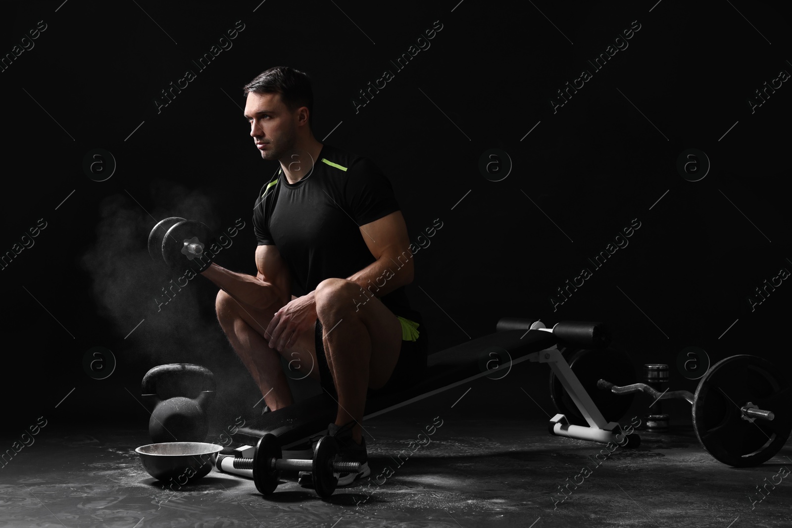 Photo of Man with talcum powder on hands training with barbell against black background