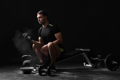 Photo of Man with talcum powder on hands training with barbell against black background