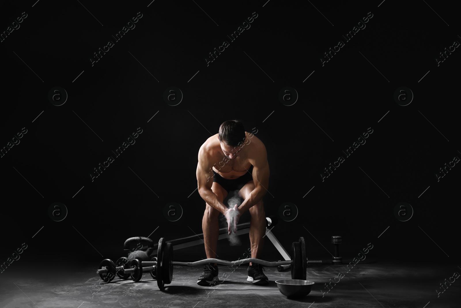 Photo of Man clapping hands with talcum powder before training with barbell on black background