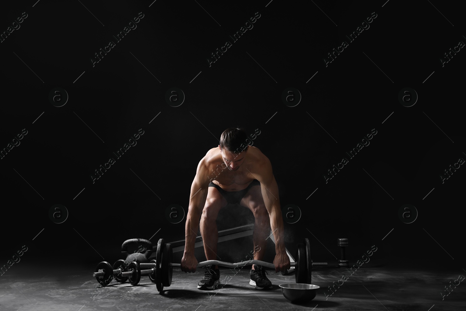 Photo of Man training with barbell against black background