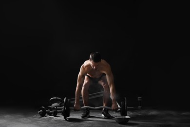 Man training with barbell against black background