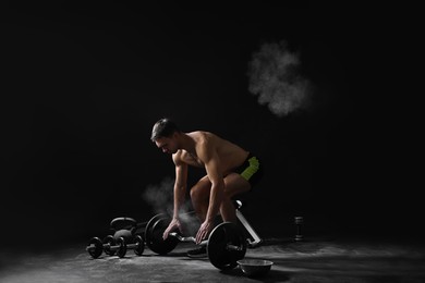 Man with talcum powder on hands training with barbell against black background