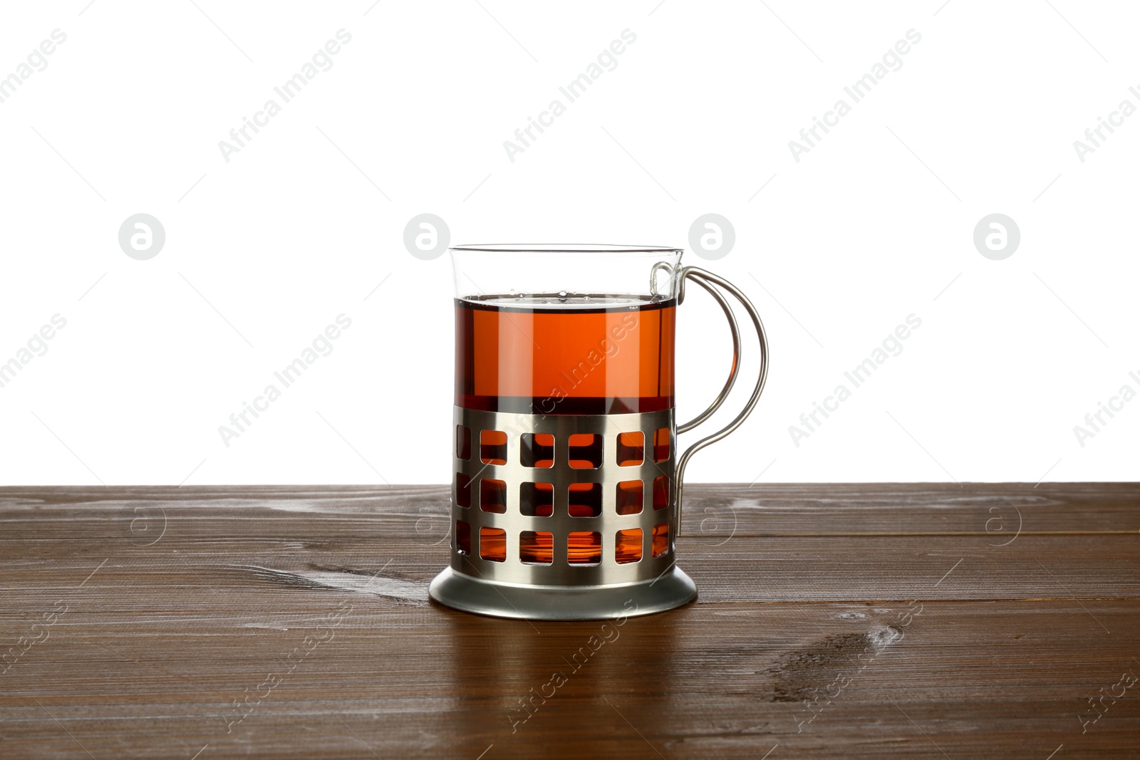 Photo of Glass of aromatic tea in holder on wooden table against white background