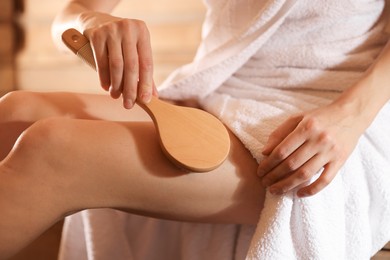 Photo of Woman massaging her leg with brush at sauna, closeup