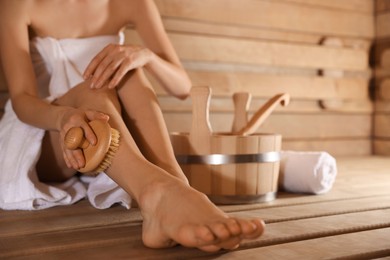 Photo of Woman massaging her leg with brush and bath supplies at sauna, closeup