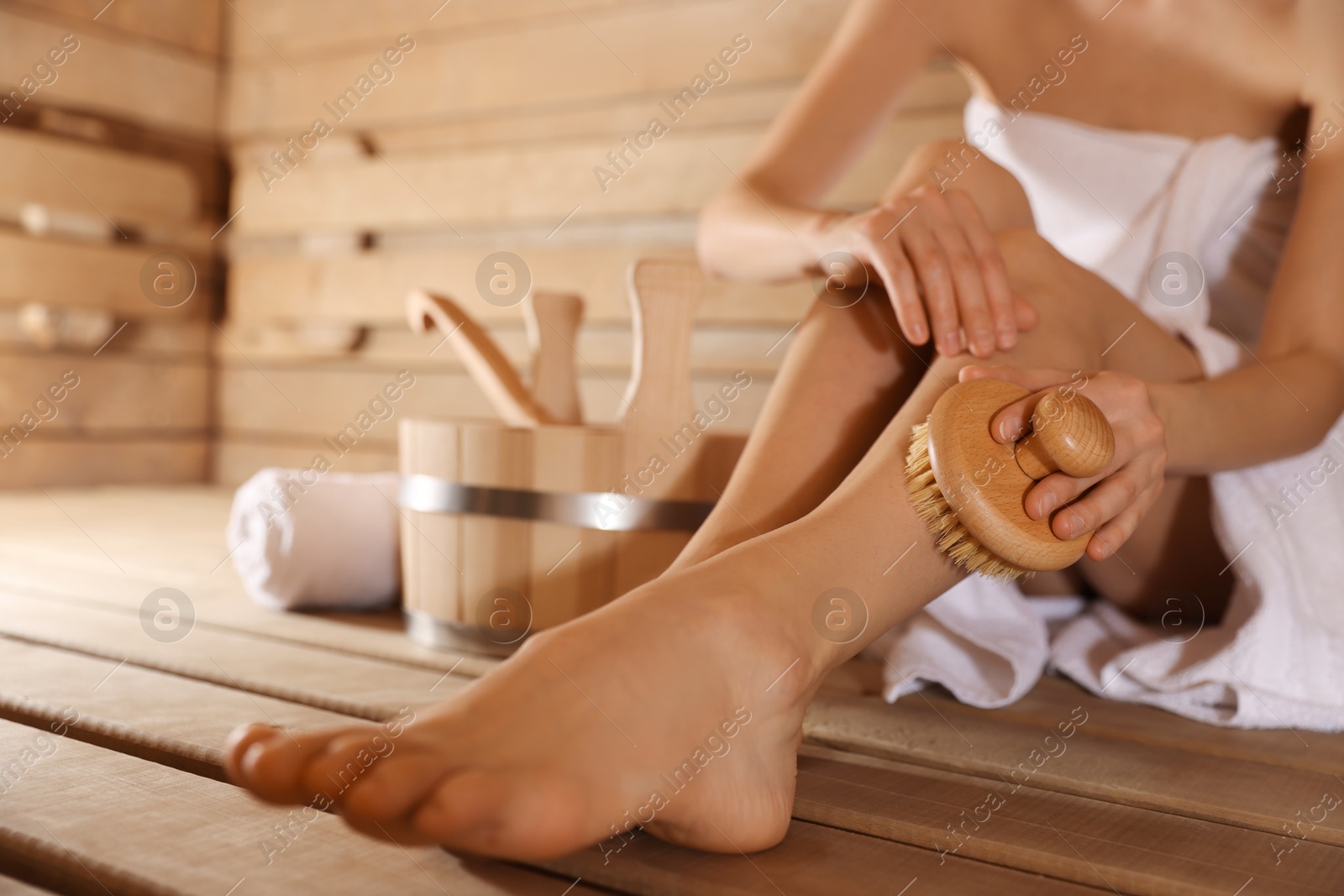 Photo of Woman massaging her leg with brush and bath supplies at sauna, closeup