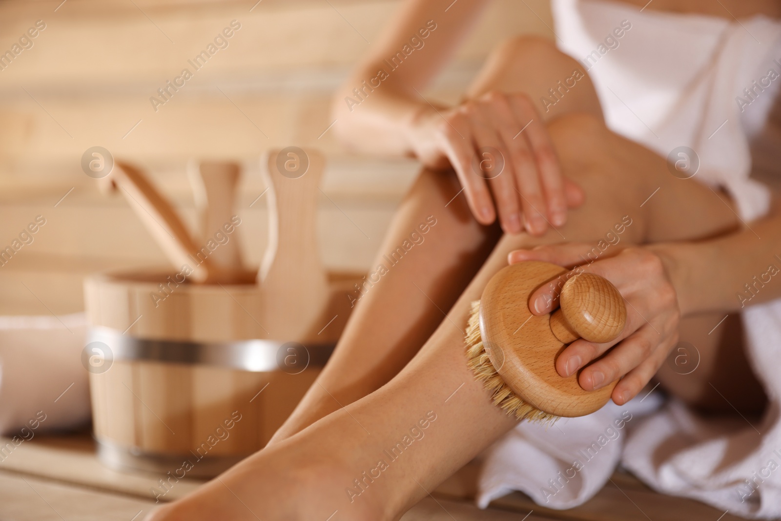 Photo of Woman massaging her leg with brush and bath supplies at sauna, closeup