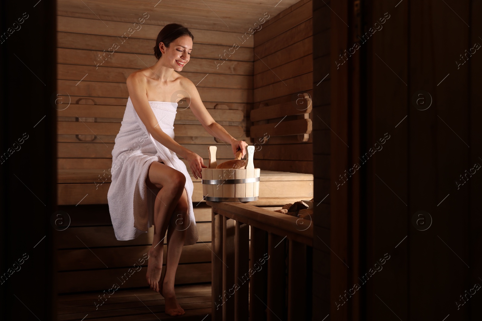 Photo of Smiling woman with bucket and ladle in sauna. Space for text