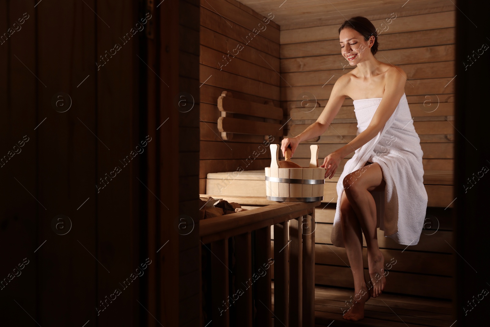 Photo of Smiling woman with bucket and ladle in sauna. Space for text