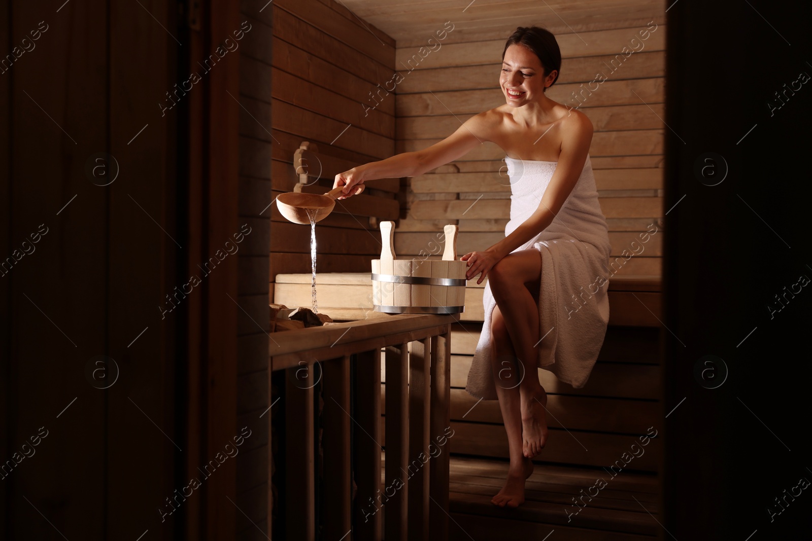 Photo of Smiling woman pouring water onto stones in sauna. Space for text