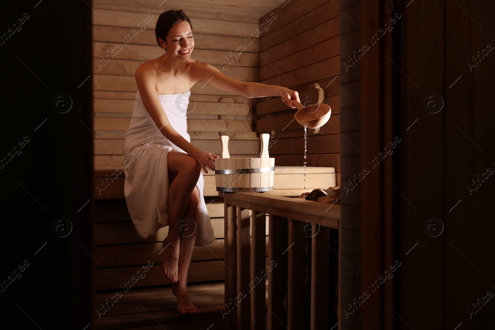 Photo of Smiling woman pouring water onto stones in sauna