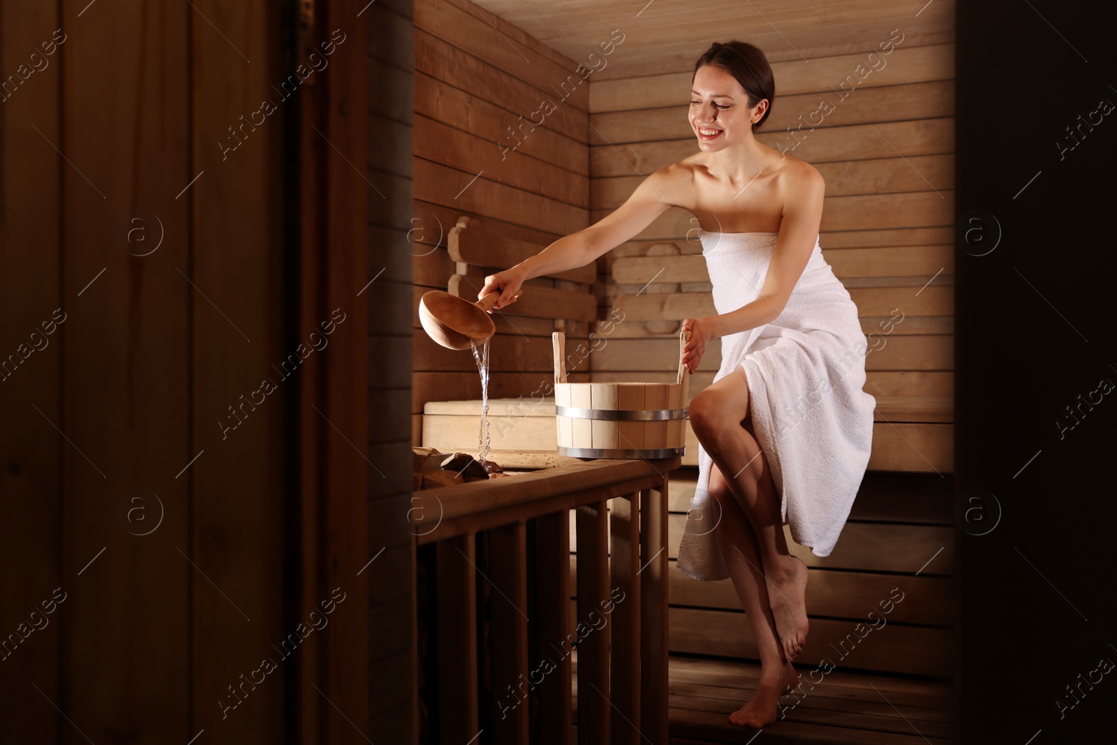 Photo of Smiling woman pouring water onto stones in sauna. Space for text